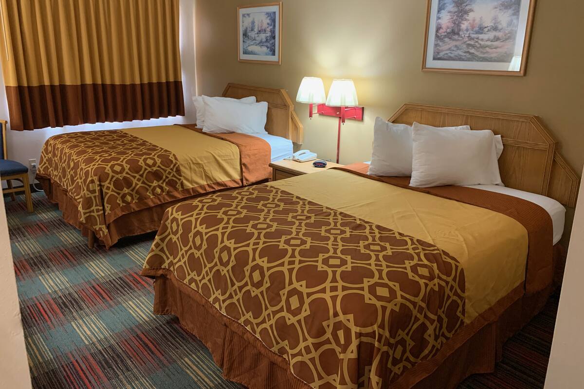 A hotel room with two beds, a chair, a desk, and two lamps.
