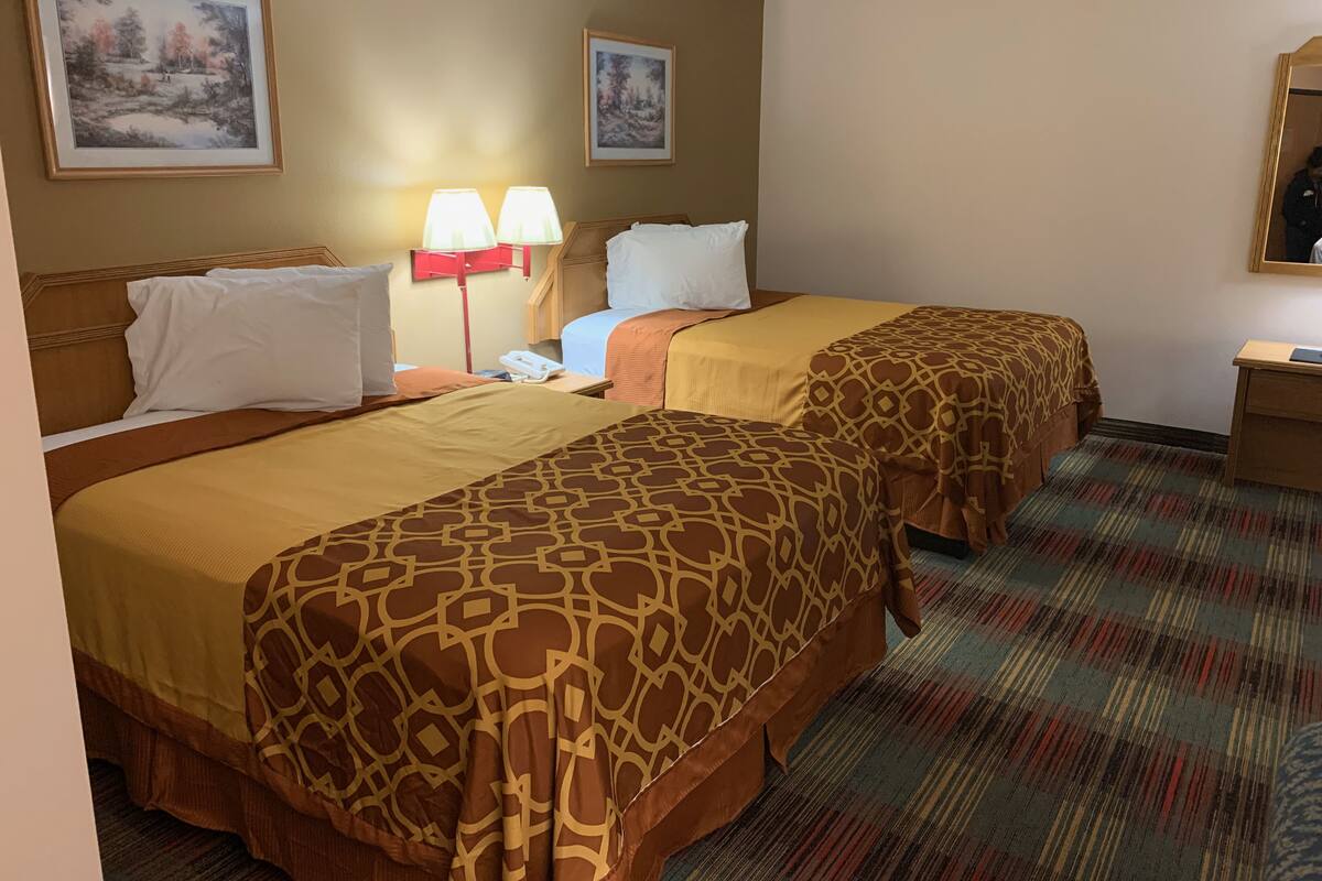 A hotel room with two beds, a nightstand, a lamp, and two framed pictures on the wall.
