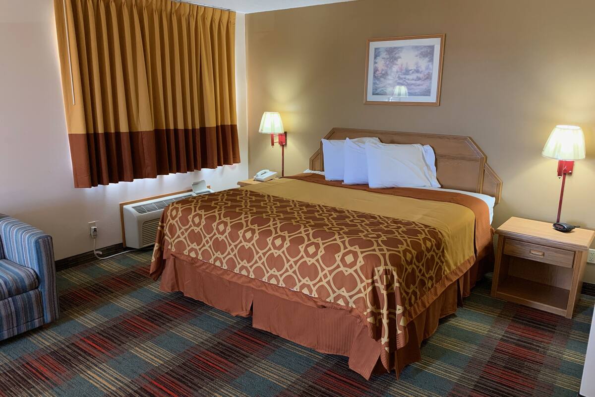A hotel room with a bed, bedside tables, a lamp, a chair, and a window with curtains.