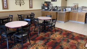 A restaurant with round tables and chairs, a coffee station, and a breakfast sign.