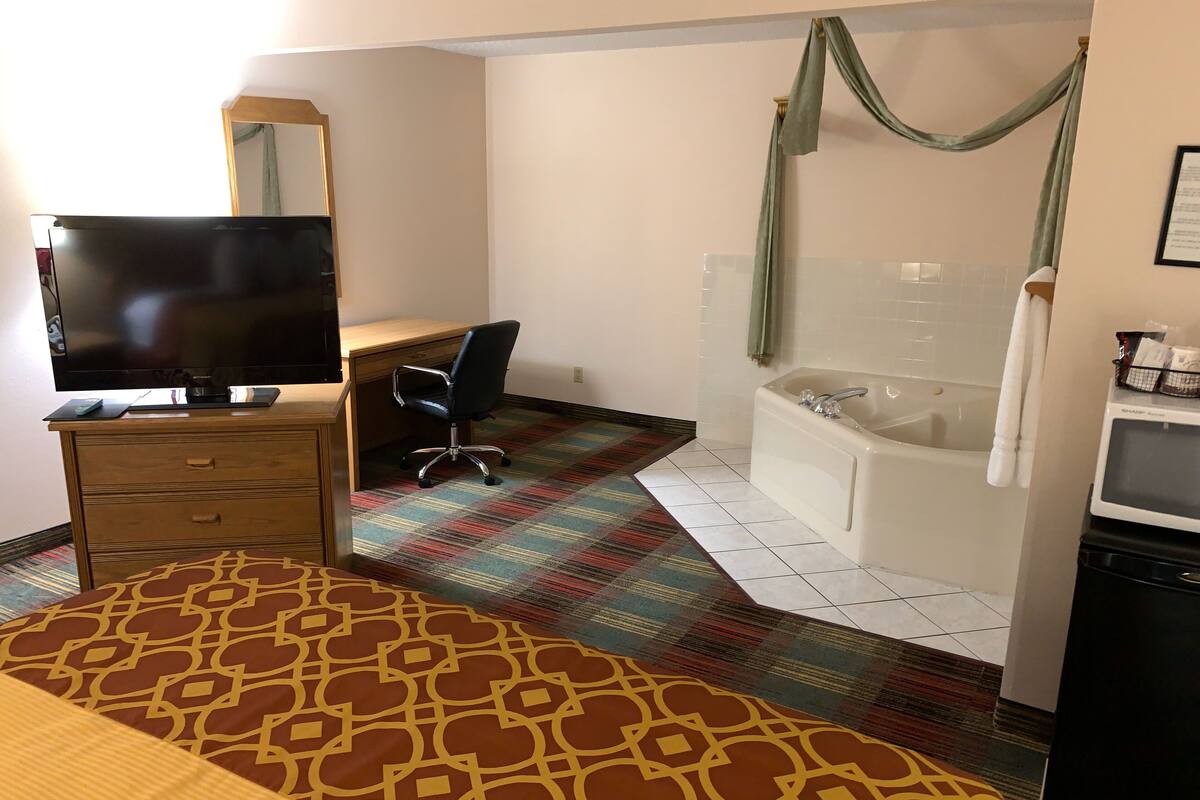 A hotel room with a bed, a desk with a chair, a television, a bathroom with a bathtub, and a shower curtain.