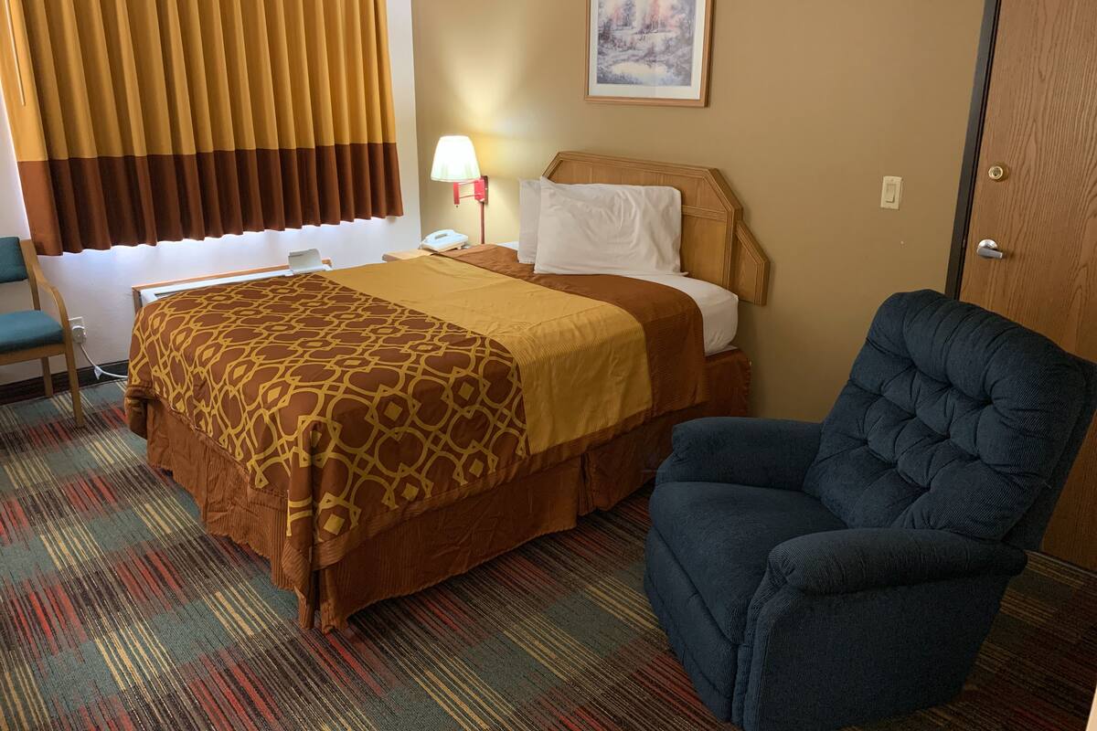 A hotel room with a bed, a chair, a lamp, and a painting on the wall.