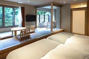Une chambre d’hôtel moderne équipée d’un canapé-lit, d’une petite table ronde avec des chaises, d’un téléviseur fixé au mur et d’une porte-fenêtre coulissante donnant sur un espace extérieur.