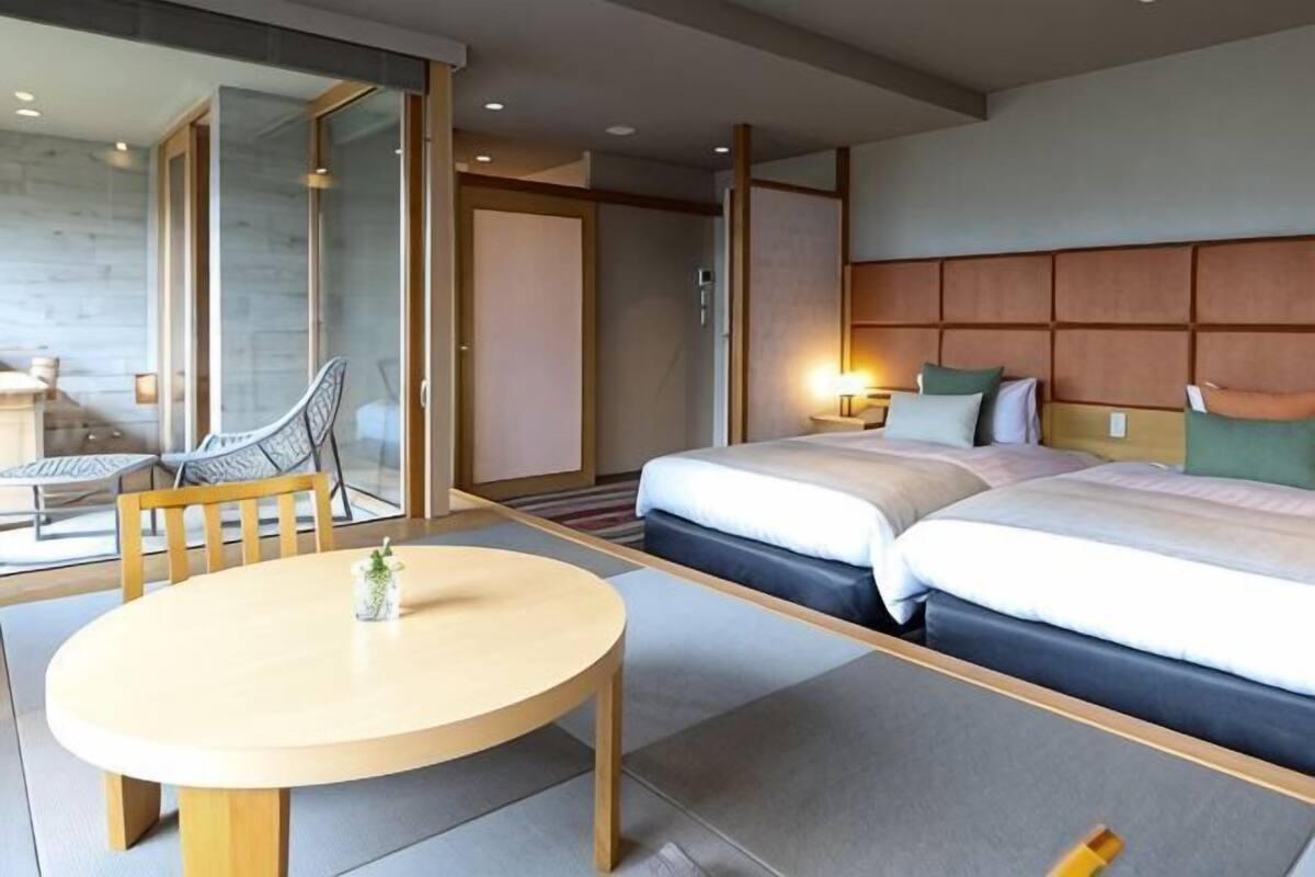 A hotel room with two beds, a round table, and a glass door leading to a balcony.