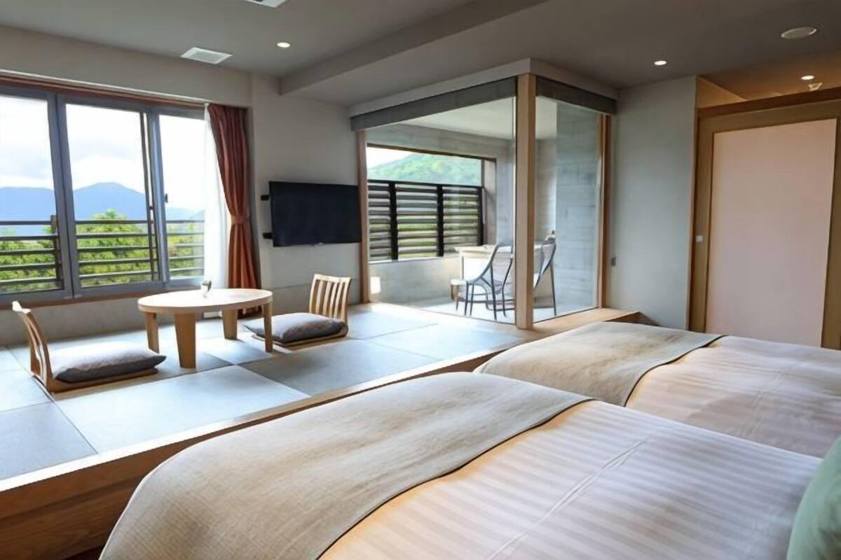 A hotel room with two beds, a balcony with a table and chairs, and a view of the mountains.