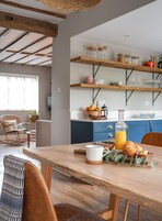 Una cocina acogedora con estantes de madera, una mesa de comedor con sillas y una preparación para el desayuno.