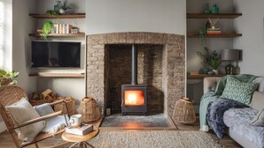 A cozy living room with a fireplace, wooden shelves, a TV, and comfortable seating. - Seascape Hideaways at Mortehoe (Woolacombe)