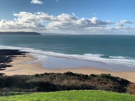 Un paisaje costero con playa, océano y una masa de tierra distante bajo un cielo parcialmente nublado.