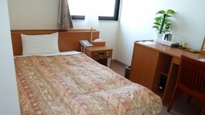Una camera d'hotel con un letto, una scrivania, una sedia, una pianta e una finestra.