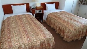Due letti singoli con biancheria a motivi floreali, un comodino con una lampada e un armadio in una camera d'albergo.