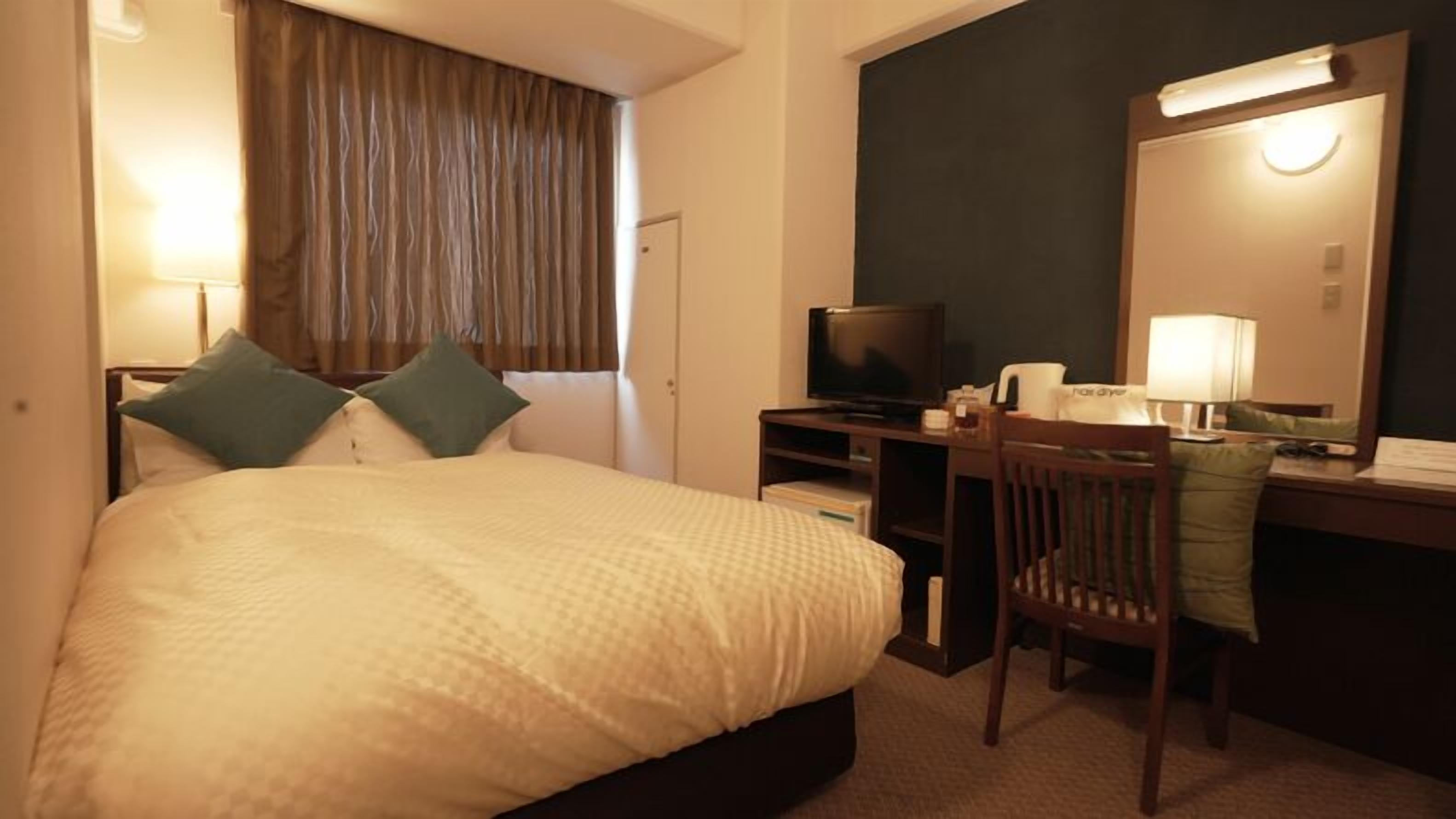 Ein Hotelzimmer mit einem Bett, einem Schreibtisch mit Fernseher, einem Sessel und einem Spiegel.