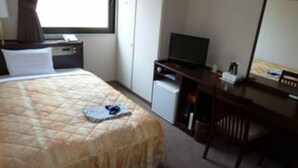 Una camera d'albergo con un letto, una scrivania, una sedia, un televisore e una finestra con tende.