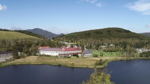 A large building with a red roof, surrounded by a lake and forested hills. - Shirakabako View Hotel (Tateshina)