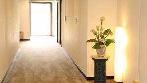 A hallway with a carpeted floor, a potted plant, and a wall-mounted light fixture. - Shirakabako View Hotel (Tateshina)