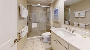 Ein modernes Badezimmer mit einer Duschkabine, einer weißen Toilette und einem großzügigen Waschtisch mit Waschbecken und Spiegel.