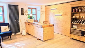 A cozy room with a wooden desk, a chair with a pillow, a radiator, a window, and shelves with jars and bottles. - Landgut Riegerbauer (Feistritztal)