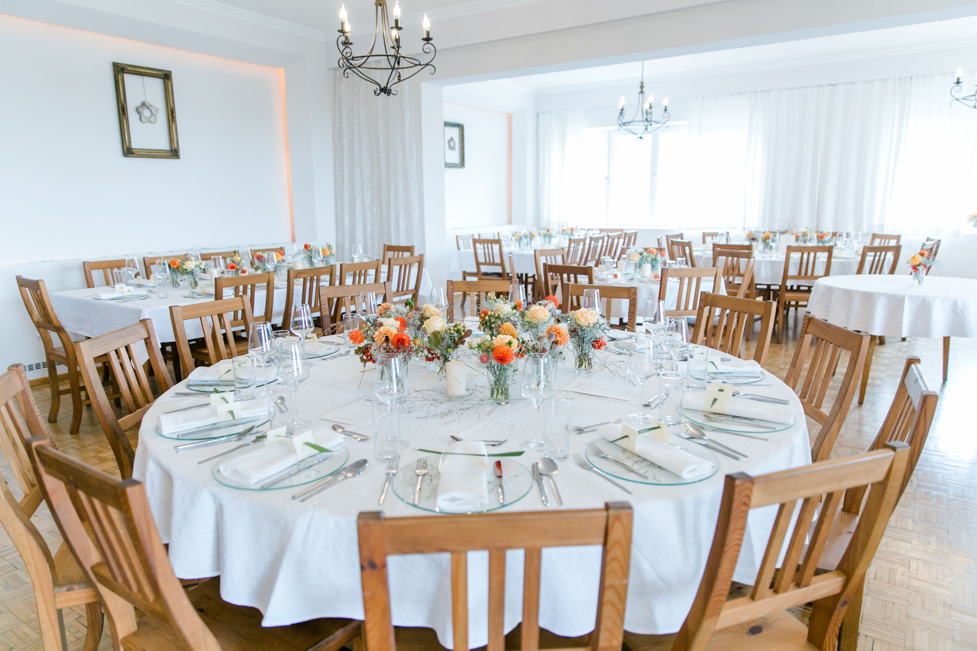 A large dining room with round tables set for a meal, wooden chairs, and floral centerpieces.