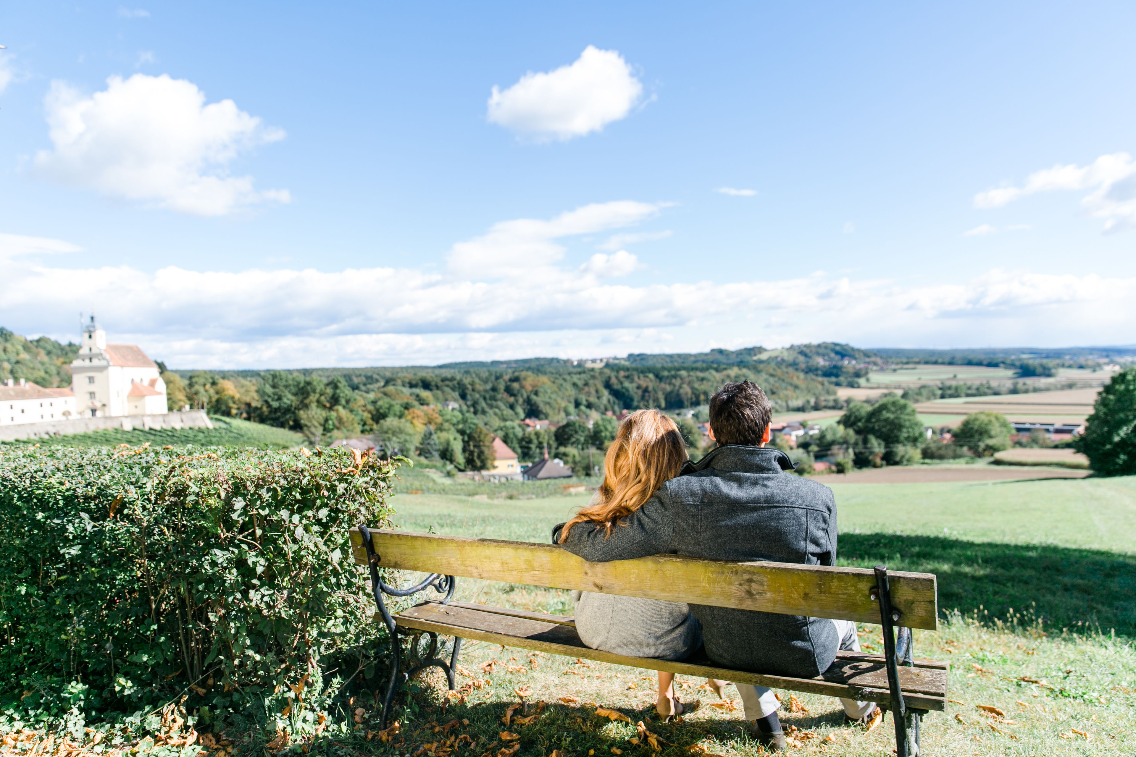 Una pareja sentada en un banco, contemplando un paisaje pintoresco con un castillo a lo lejos.