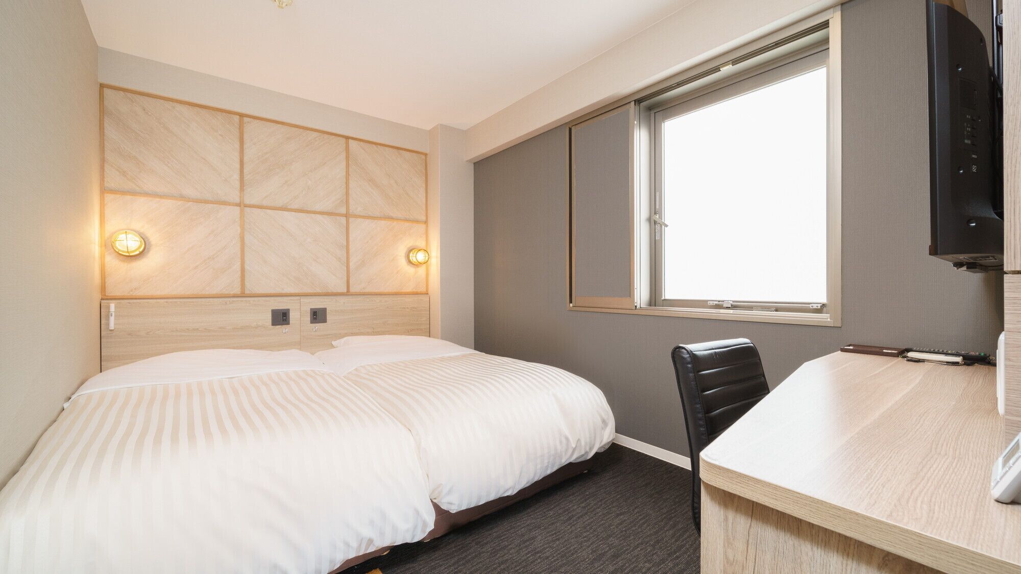 A hotel room with a bed, a desk, a chair, a television, and a window.