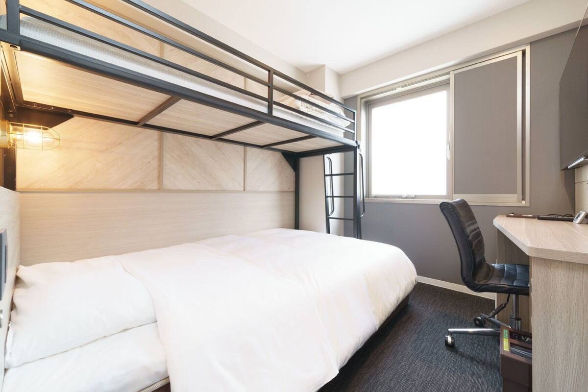 A bunk bed with a desk and chair, a window, and a headboard with built-in lighting.