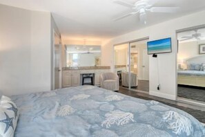 A bedroom with a bed, a television, and a sliding door leading to a bathroom. - Luxury Gulf-Side Retreat | Remodeled 2-Bedroom Condo | Siesta Key (Sarasota)