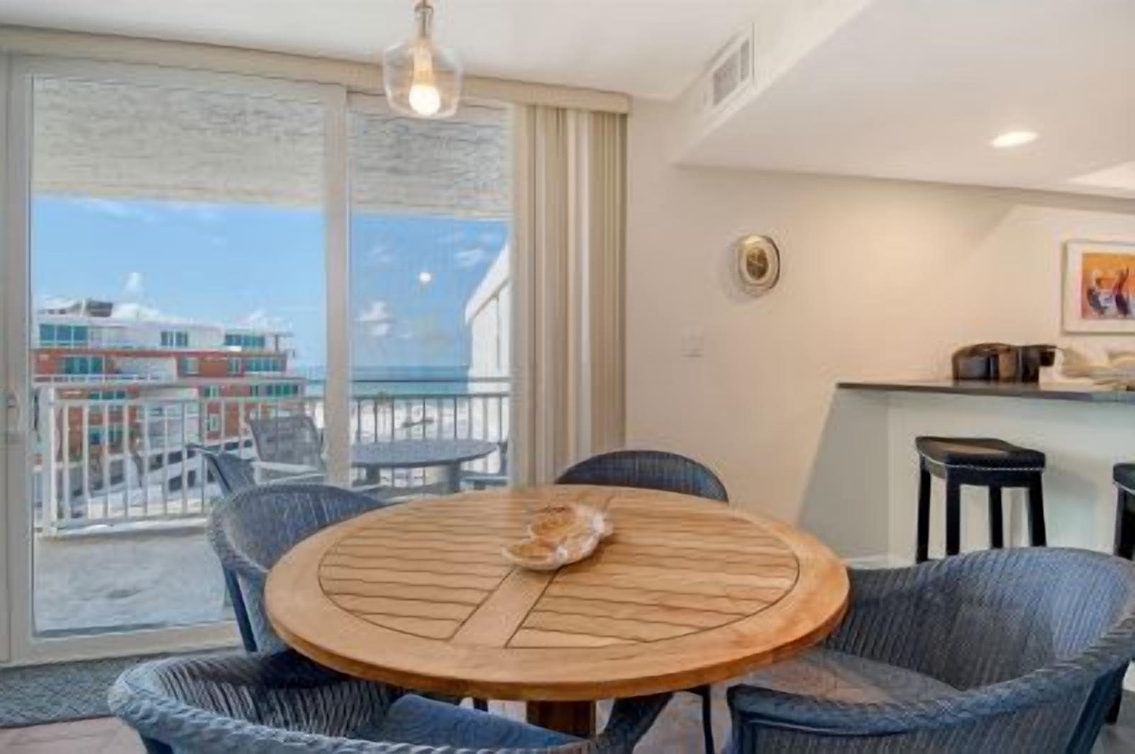 Una mesa redonda de madera con sillas en una habitación que tiene vista a edificios y un balcón.
