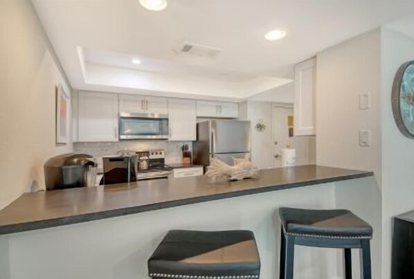 A modern kitchen with a central island, bar stools, and stainless steel appliances. - Luxury Gulf-Side Retreat | Remodeled 2-Bedroom Condo | Siesta Key (Sarasota)