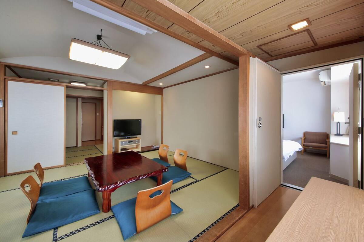 Une pièce de style japonais traditionnel, avec un sol recouvert de tatamis, une petite table en bois et un téléviseur.