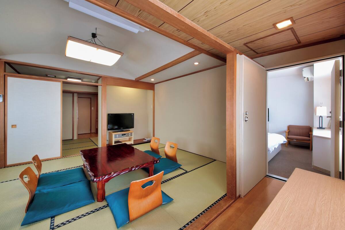 Une pièce de style japonais traditionnel, avec un sol recouvert de tatamis, une table en bois et un téléviseur.