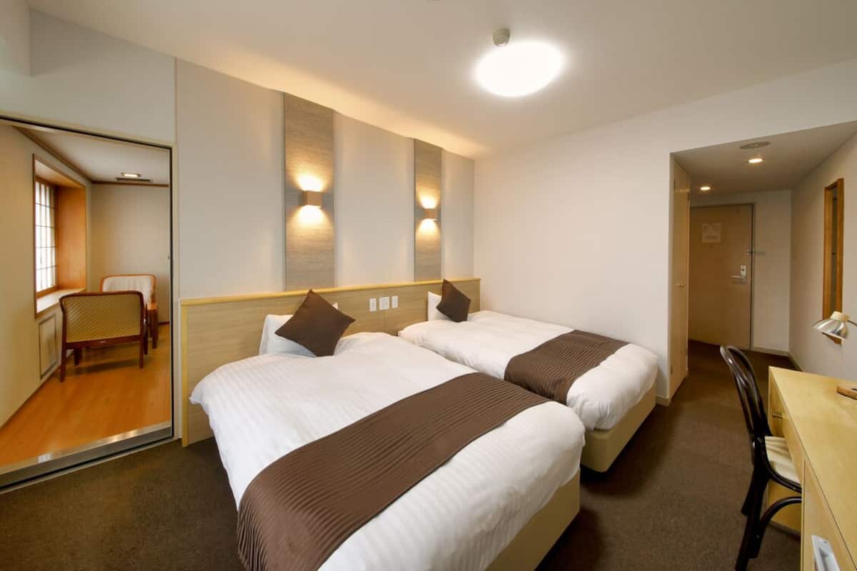 Une chambre d’hôtel avec deux lits, un bureau, une chaise et un miroir.