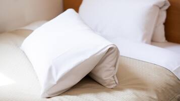 A neatly made bed with white bedding and a beige pillow.