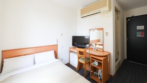 Una habitación de hotel con una cama, un escritorio con televisor, un espejo, un refrigerador pequeño y una puerta negra con un cartel.