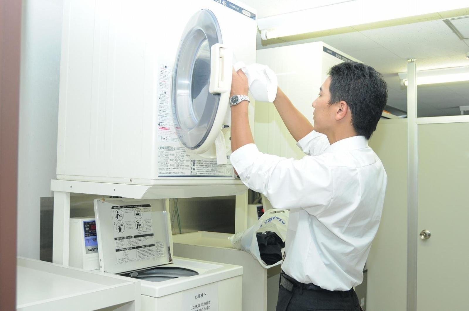 A person operating a large industrial washing machine in a clean, well-lit room with a door in the background.