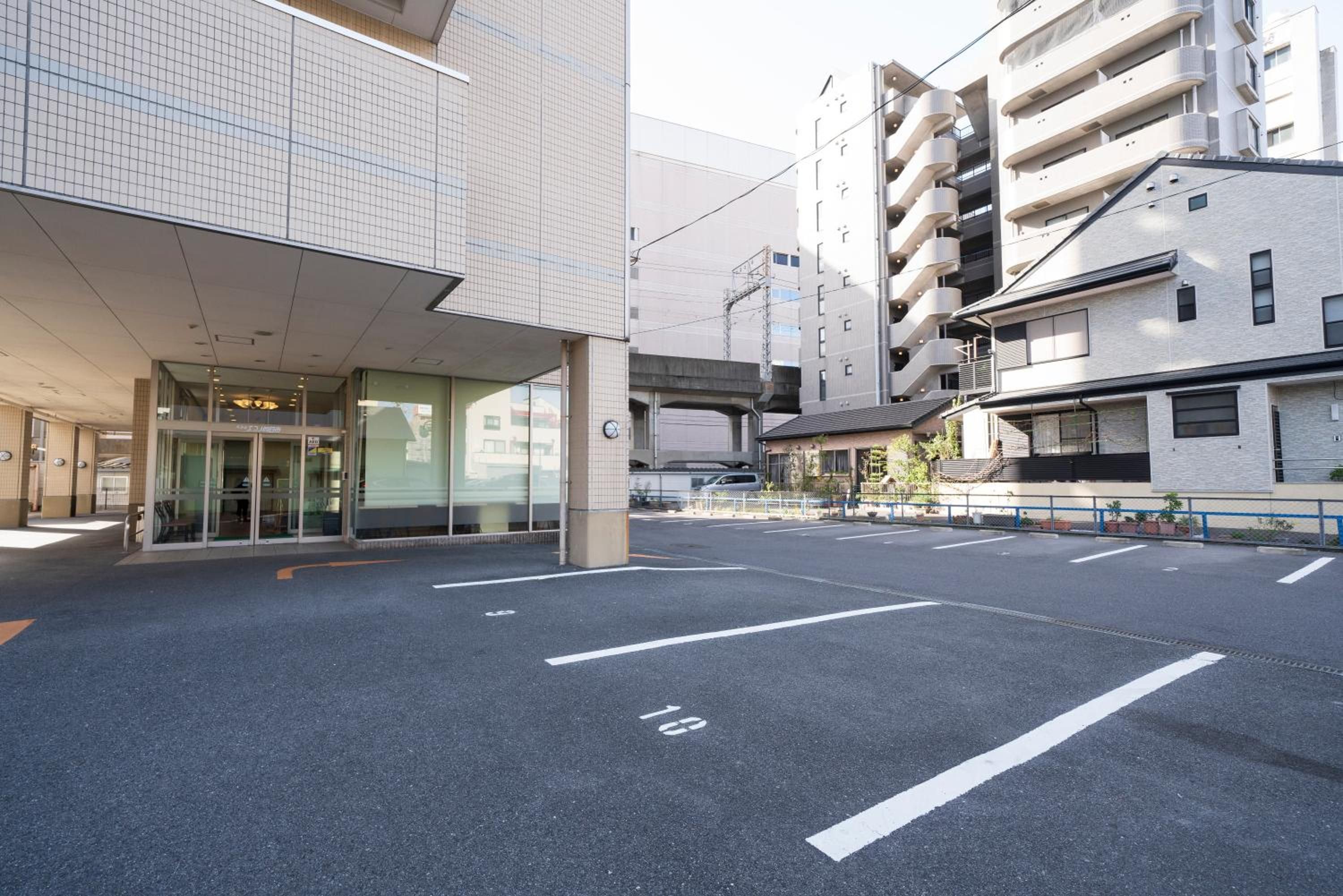 A building with a covered entrance, a parking lot with marked spaces, and a multi-story residential building in the background.