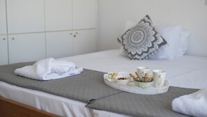 A neatly made bed with a gray quilted bedspread, a folded white towel, and a tray with breakfast items including cereal, a bowl of nuts, and two mugs. - Villa Del Nonno (Rhodes)