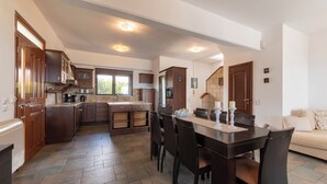 A spacious kitchen with a central island, dark wooden cabinets, and a dining area with a table and chairs. - Villa Del Nonno (Rhodes)
