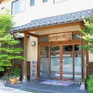Edificio japonés tradicional con tejado de tejas, entrada de madera y señalización.