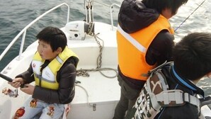 Um barco com duas pessoas usando coletes salva-vidas, uma delas segurando uma vara de pesca.
