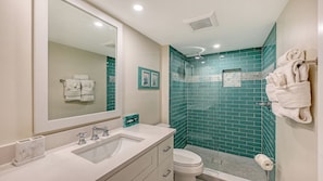 A bathroom with a white sink, a mirror, a toilet, and a shower area with green tiles.