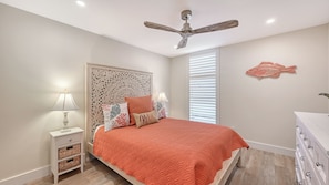 A bedroom with a bed, nightstands, a ceiling fan, a window with blinds, and a wall decoration. - House Of The Sun #302GS (Sarasota)