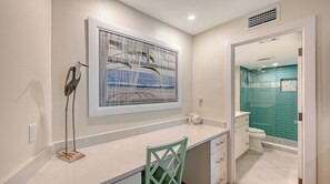 A bathroom with a shower, a toilet, and a sink. There is a framed picture on the wall and a bird sculpture on the counter. - House Of The Sun #302GS (Sarasota)