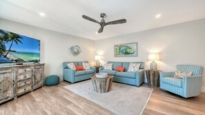 A living room with a television, two sofas, a coffee table, a ceiling fan, and a decorative wall piece. - House Of The Sun #302GS (Sarasota)