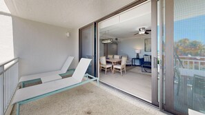 Ein Balkon mit Glastisch und Stühlen, eine Schiebetür zu einem Essbereich mit einer Deckenleuchte und einem Deckenventilator.