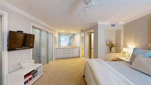 A hotel room with a bed, a TV, a bathroom with a mirror, and a hallway leading to another room.