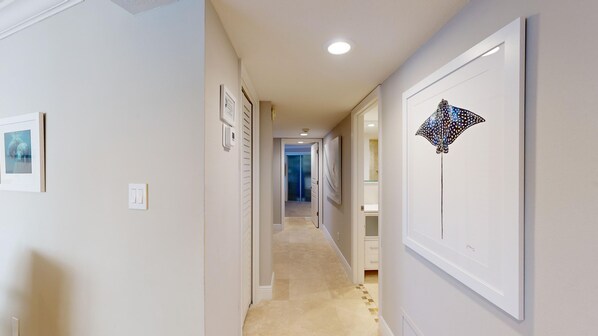 A hallway with framed artwork on the walls, a light switch, and a door leading to a room.