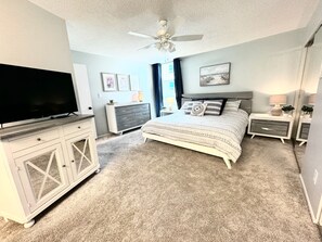 Quarto com cama, televisão, penteadeira e ventilador de teto.
