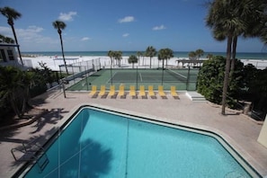 Área de piscina com quadra de tênis e vista para a praia.