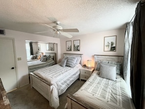 A bedroom with two beds, a ceiling fan, bedside lamps, and framed artwork on the walls.