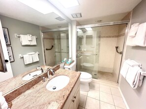 Ein Badezimmer mit einem Doppelwaschbecken, einer Toilette, einer Duschkabine aus Glas und einem großen Spiegel.