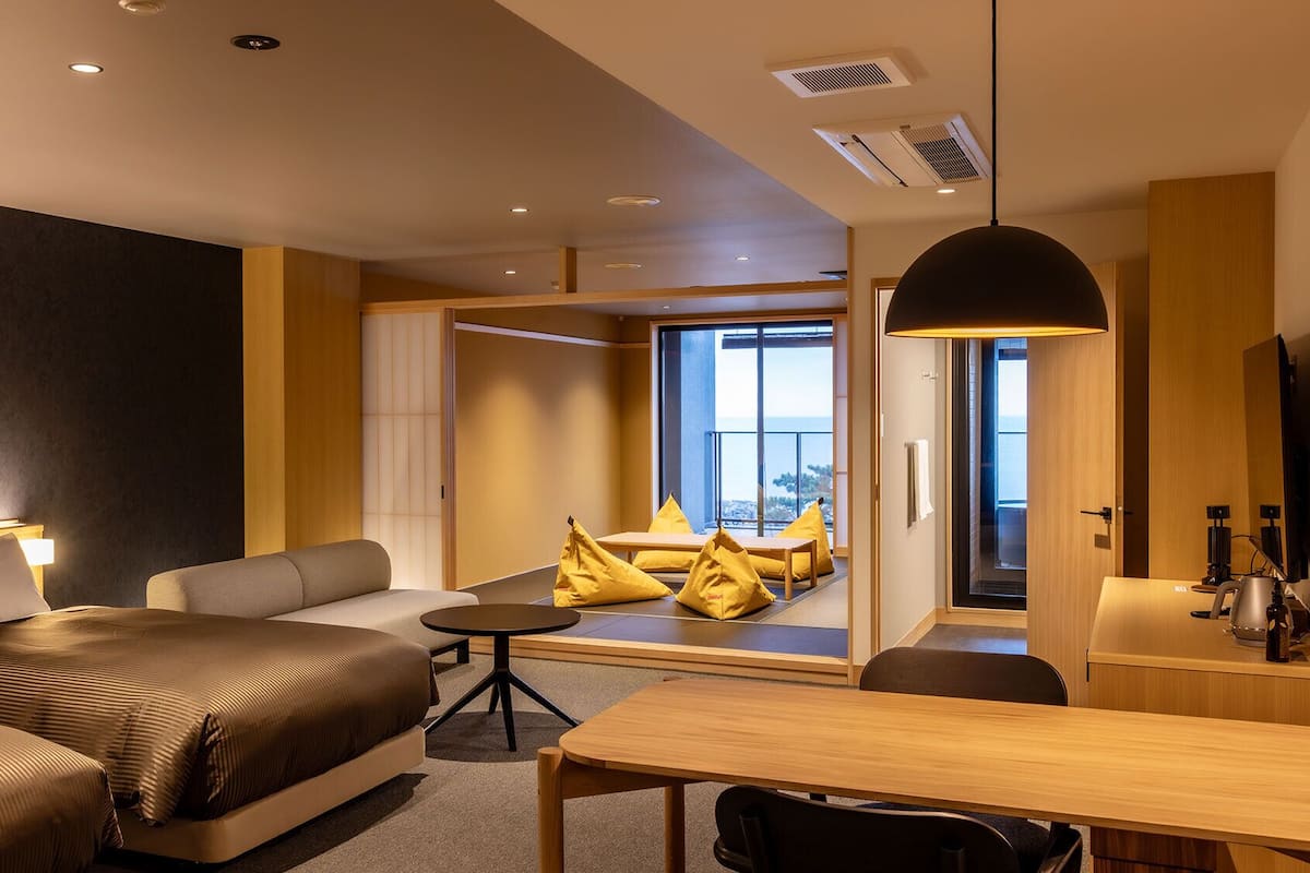 Habitación de hotel moderna con cama, sofá, mesa de comedor y vistas al exterior.